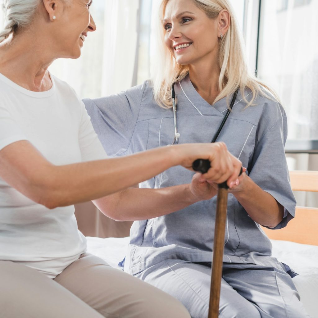nurse and happy senior woman with cane smiling each other in nursing home