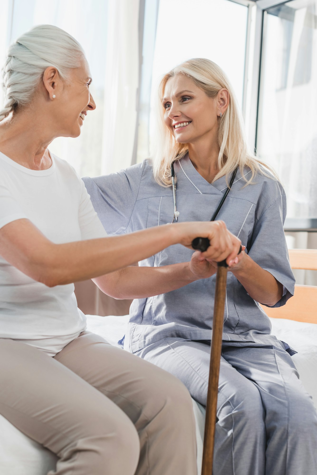 nurse and happy senior woman with cane smiling each other in nursing home