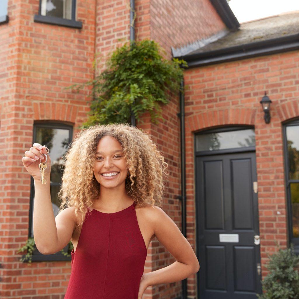 Portrait Of Excited Young Woman Standing Outside New Home Holding Keys
